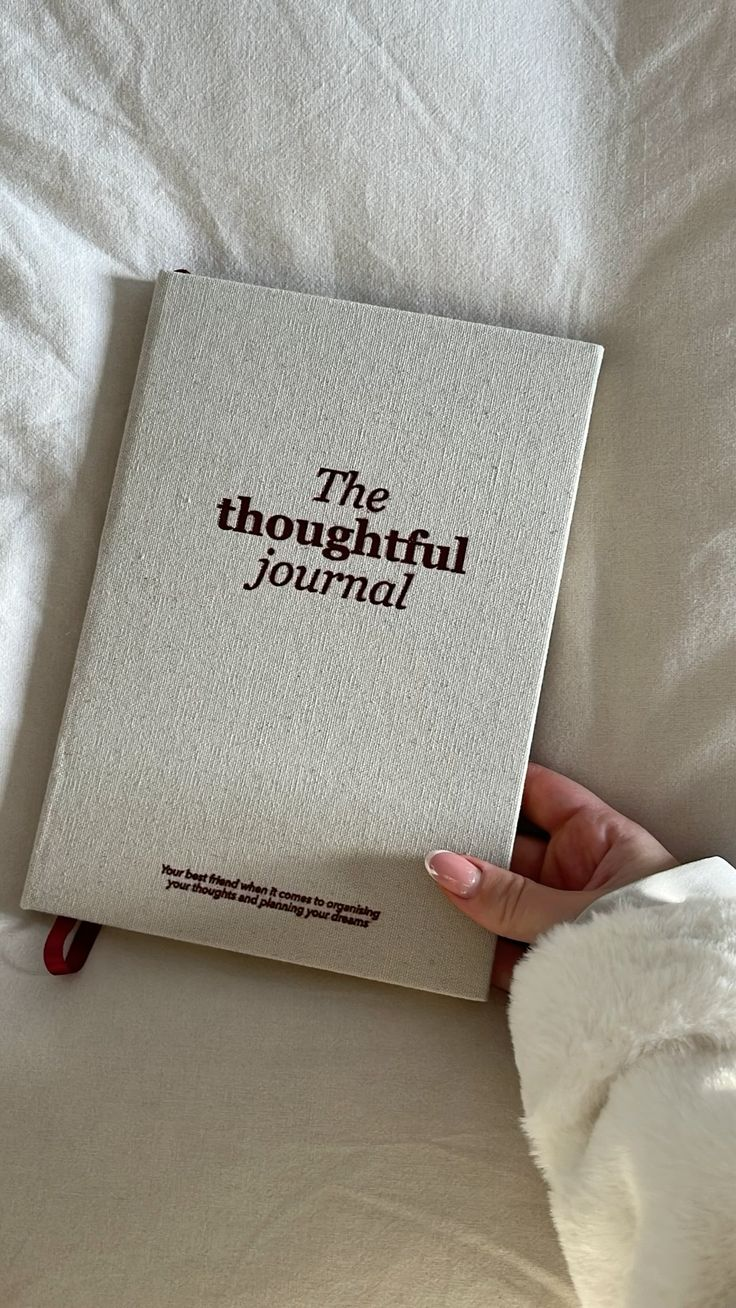 Hand resting on a linen-bound journal on soft white bedding